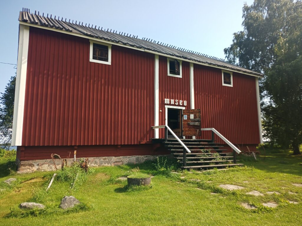 En hög, rödmålad träbyggnad med vita knutar i två våningar, med texten "Museo" i frakturstil ovanför dörren. Endast övervåningen har fönster.