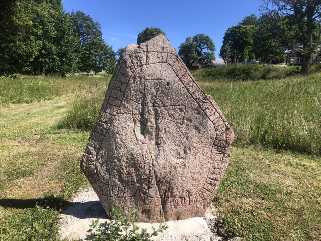 Bilden visar en runsten rest ute i landskapet.