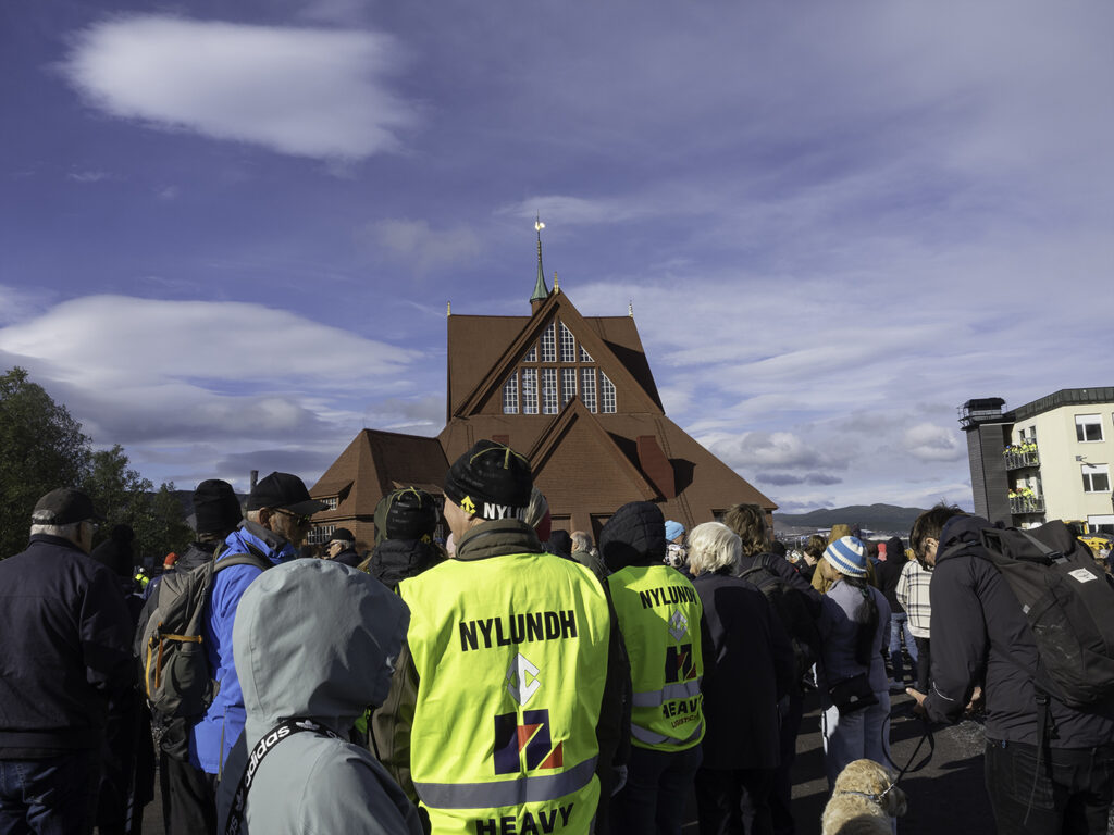 Kiruna kyrka flyttas. En folksamling står framför kyrkan, som är lastad på trailers och snart skall börja rulla.