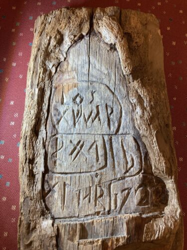 En stående träbit med en utskuren platta med tre rader runor på.