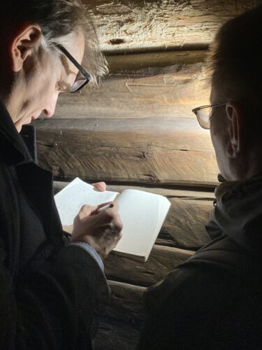 Två män står framför en upplyst trävägg och dokumenterar i en anteckningsbok.