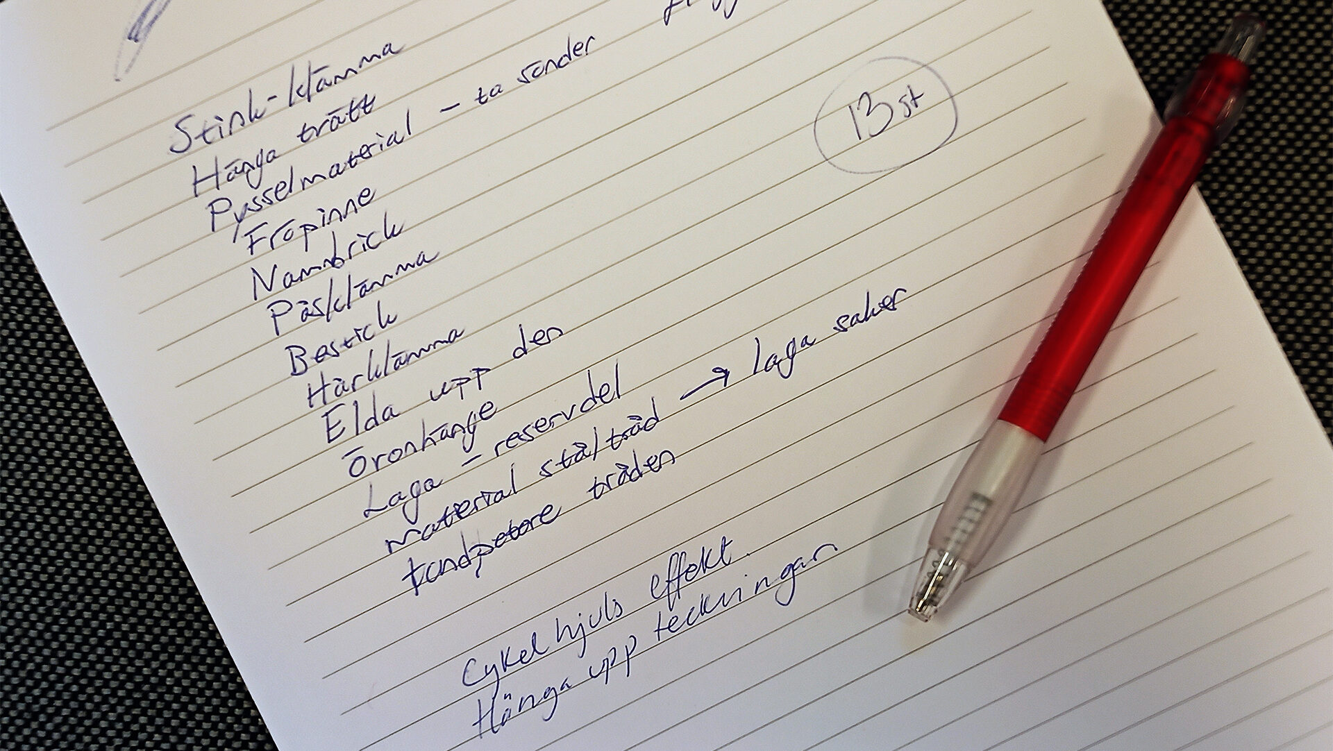 En penna ligger på ett randigt A4-papper med en skriven lista med förslag till vad man kan göra med en klädnypa. Några exempel är: "Elda upp", "Stinkklämma", "Öronhänge" och "Bestick".