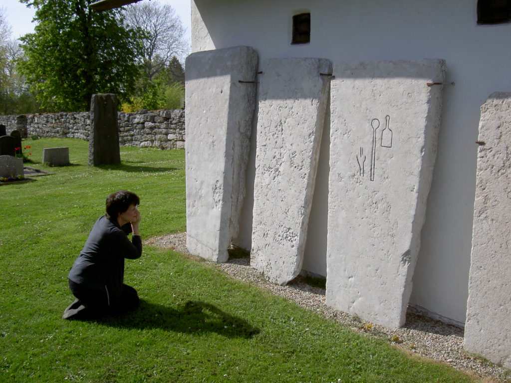 Bilden visar en kvinna på knä som fotograferar framför tre gravhällar som står resta mot en bod