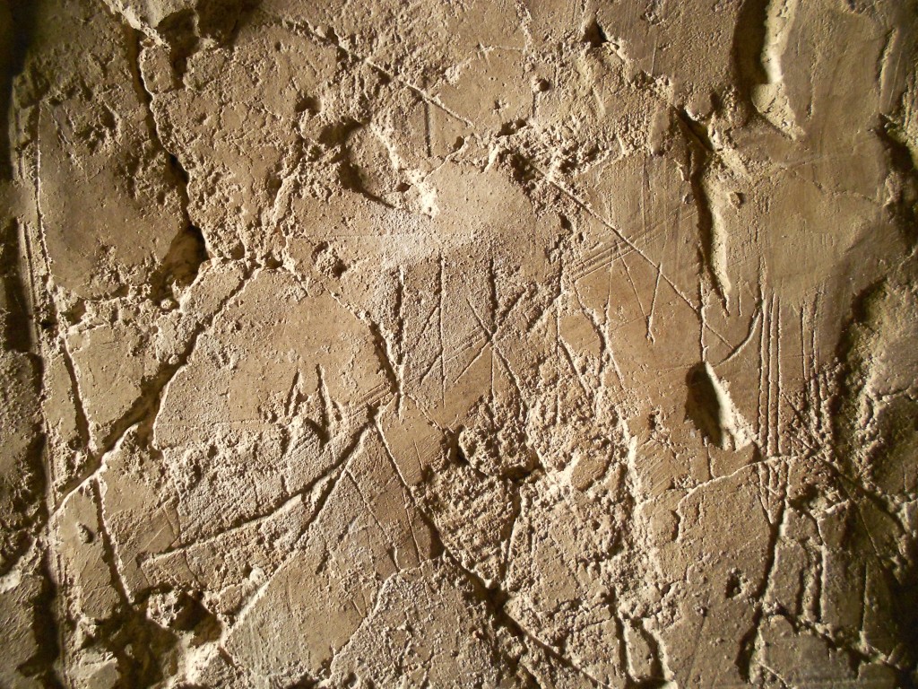 Bilden visar en del av en putsad väggyta med runor och andra ristningar