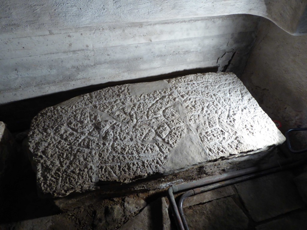 Bilden visar en gravhäll med runor och ornamentik i mörkerbelysning