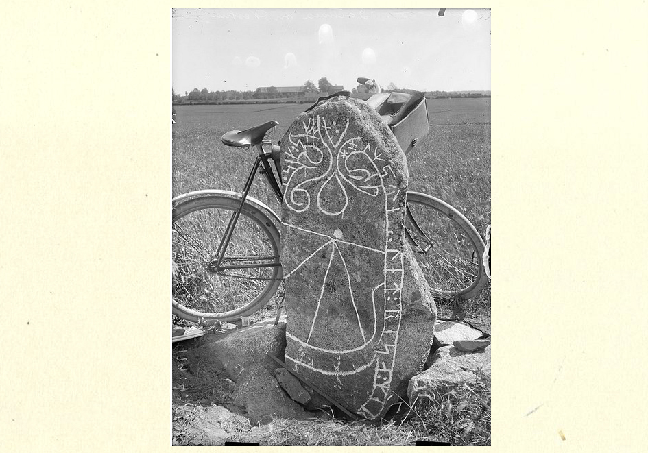 Bilden visar ett äldre fotografi av en runsten och en cykel som står lutad mot baksidan av denna