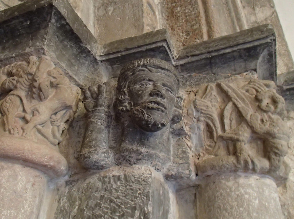 Bilden visar en medeltida skulptur av ett manshuvud med en huvudbonad försedd med en enskrift