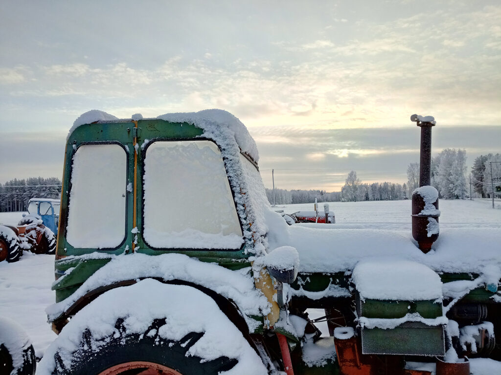 Gamla traktor en snöig, mulen novemberdag. Det ligger ett lätt snötäcke på traktorerna, som också har igenisade rutor.