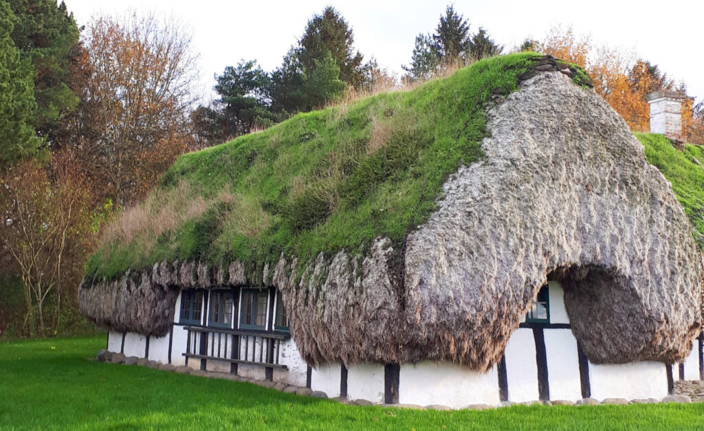 Bilden visar ett äldre stenhus med gräs på taket.