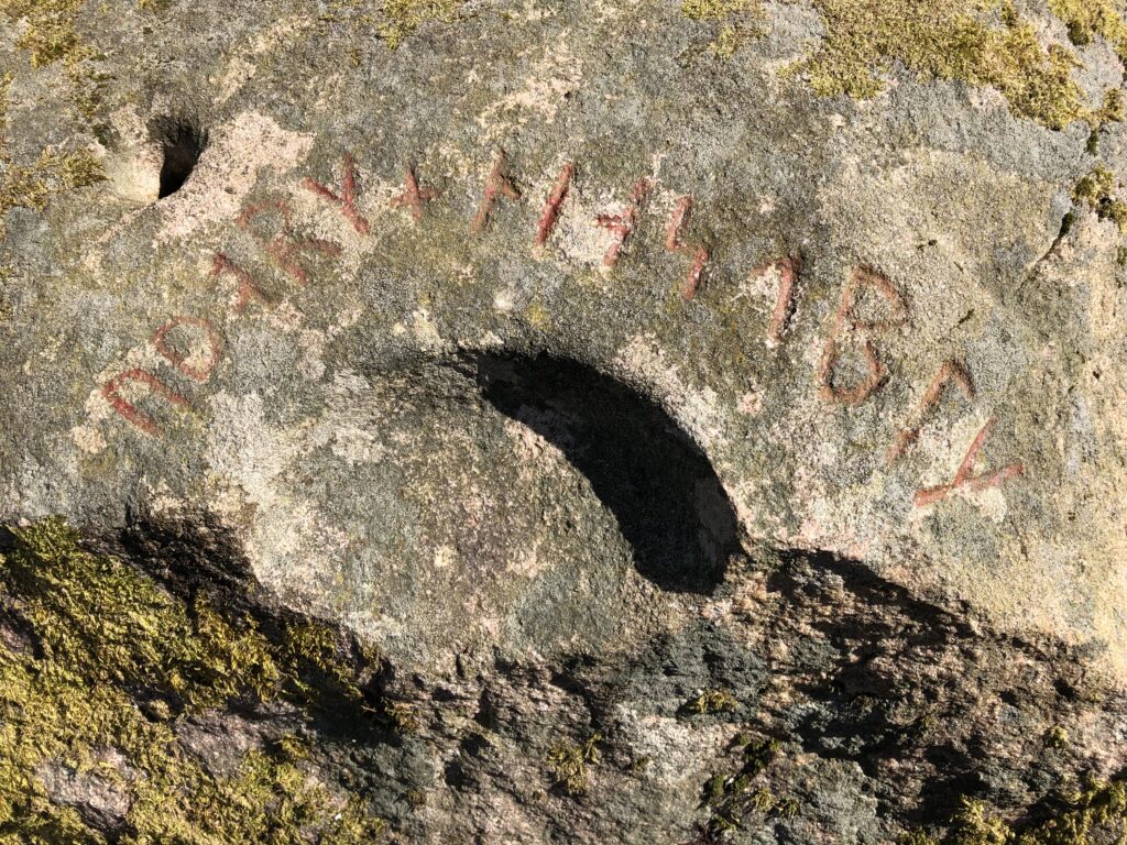 Bilden visar en runrad som står i en halvcirkel kring en skålformig uthuggning i ett stenblock.