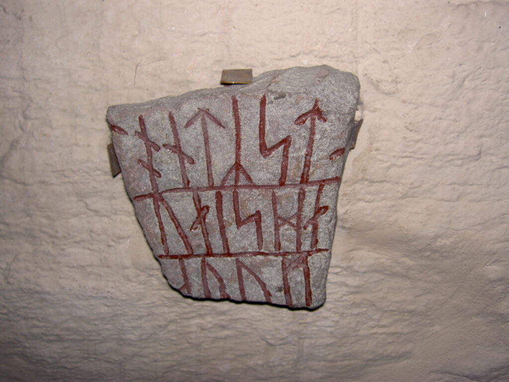 Bilden visar ett runstensfragment med runor i tre vågräta rader.
