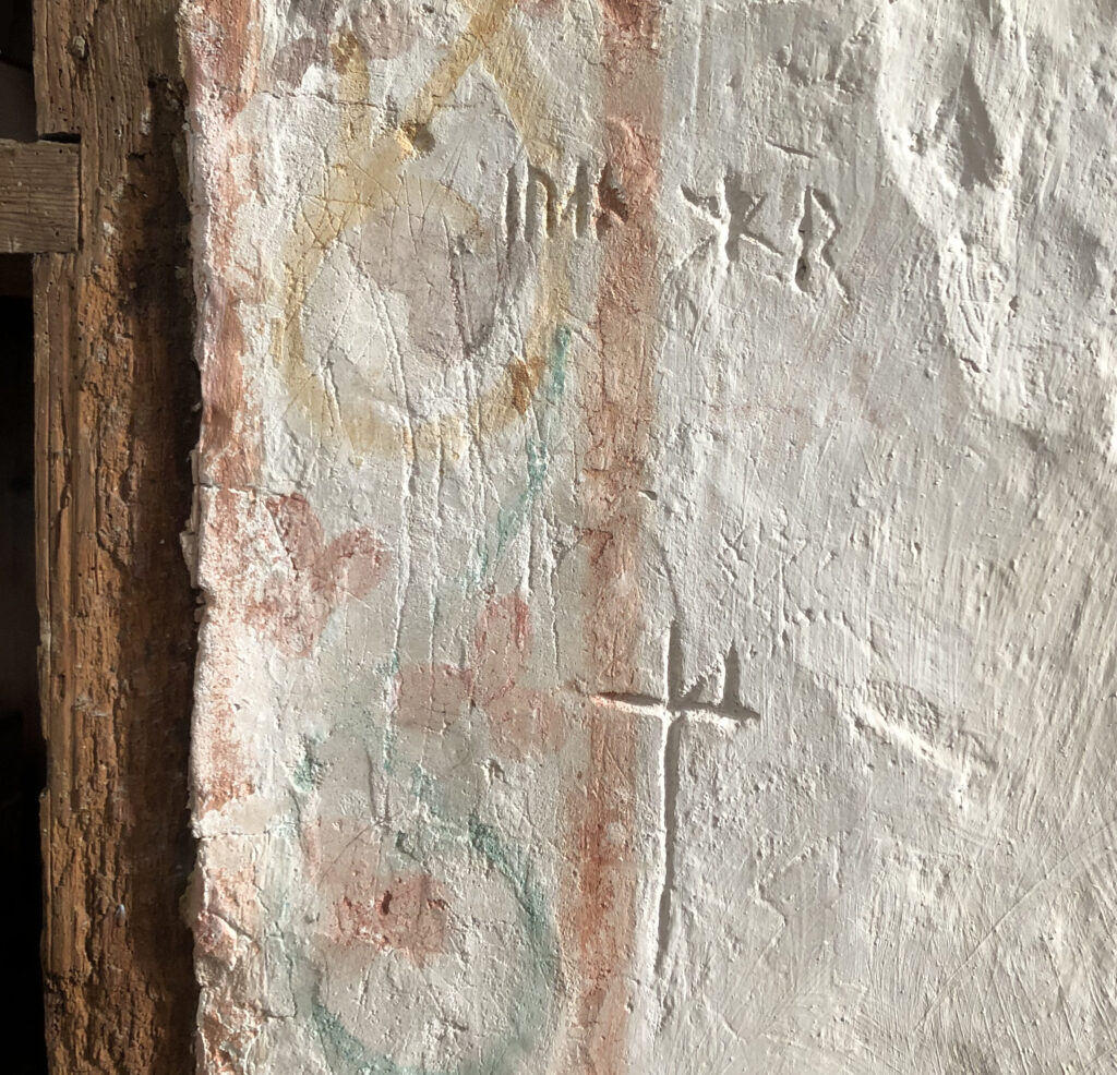 Bilden visar en kyrkvägg med ristningar, bland annat runor och bomärken.