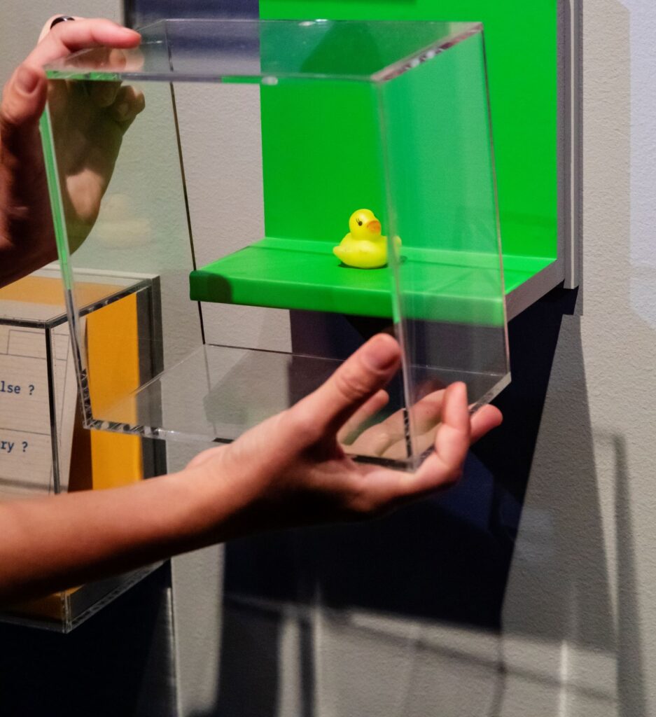 Händer som lyfter av en glasmonter där det finns en gul gummianka.