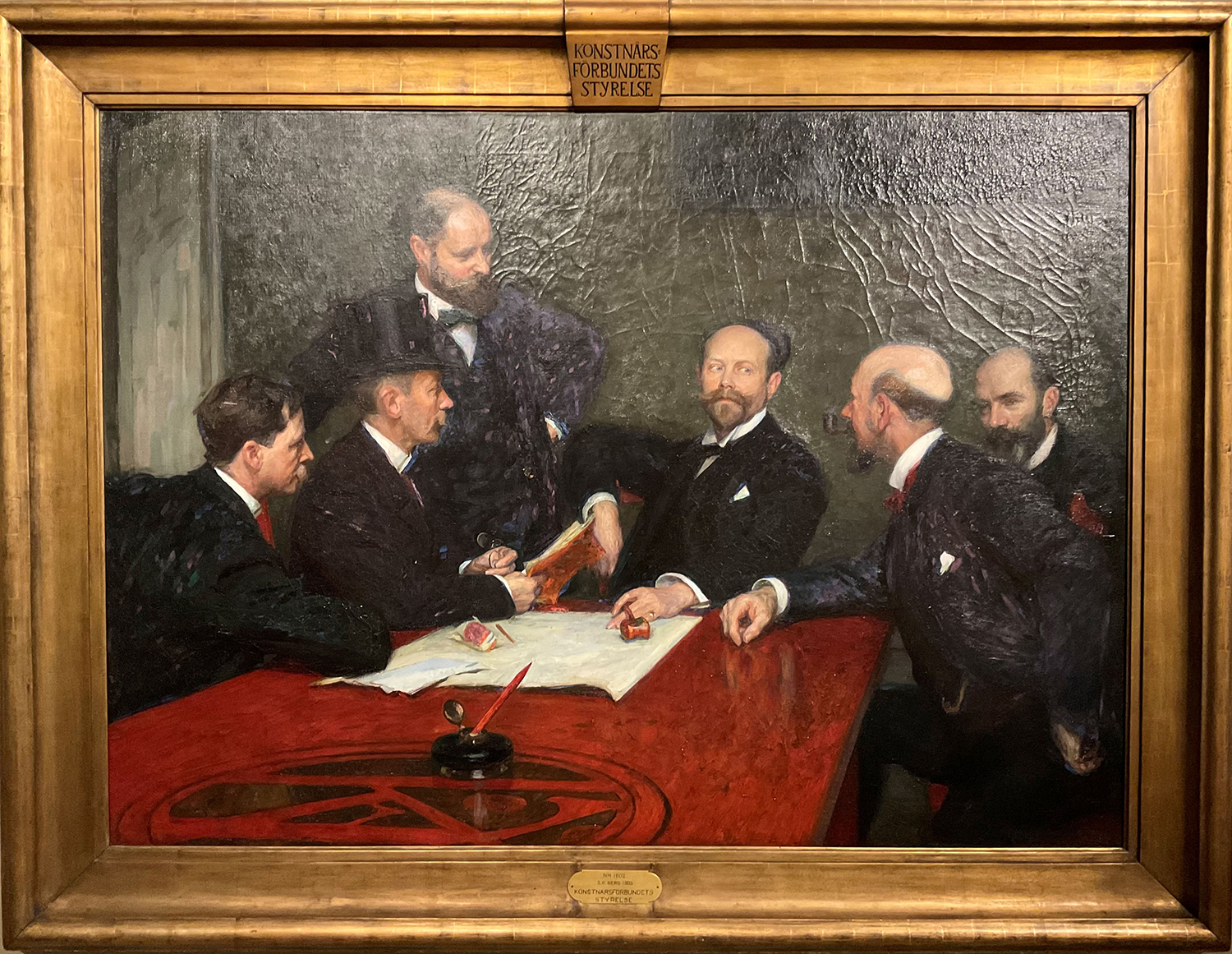 Stor målning med guldram av fem män runt ett brunt stort bord. Fyra av dem sitter, en står och en har hög hatt. En man håller en ordförandeklubba.