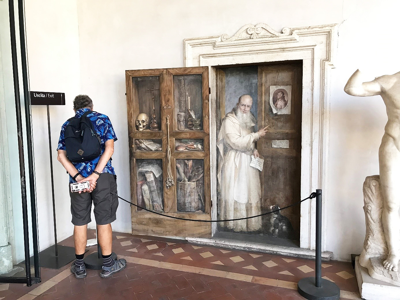 Bild av en besökare inne på ett museum som tittar på en realistisk väggmålning, en så kallad trompe l’oeil-målning på Museet Diocletianus termer i Rom.