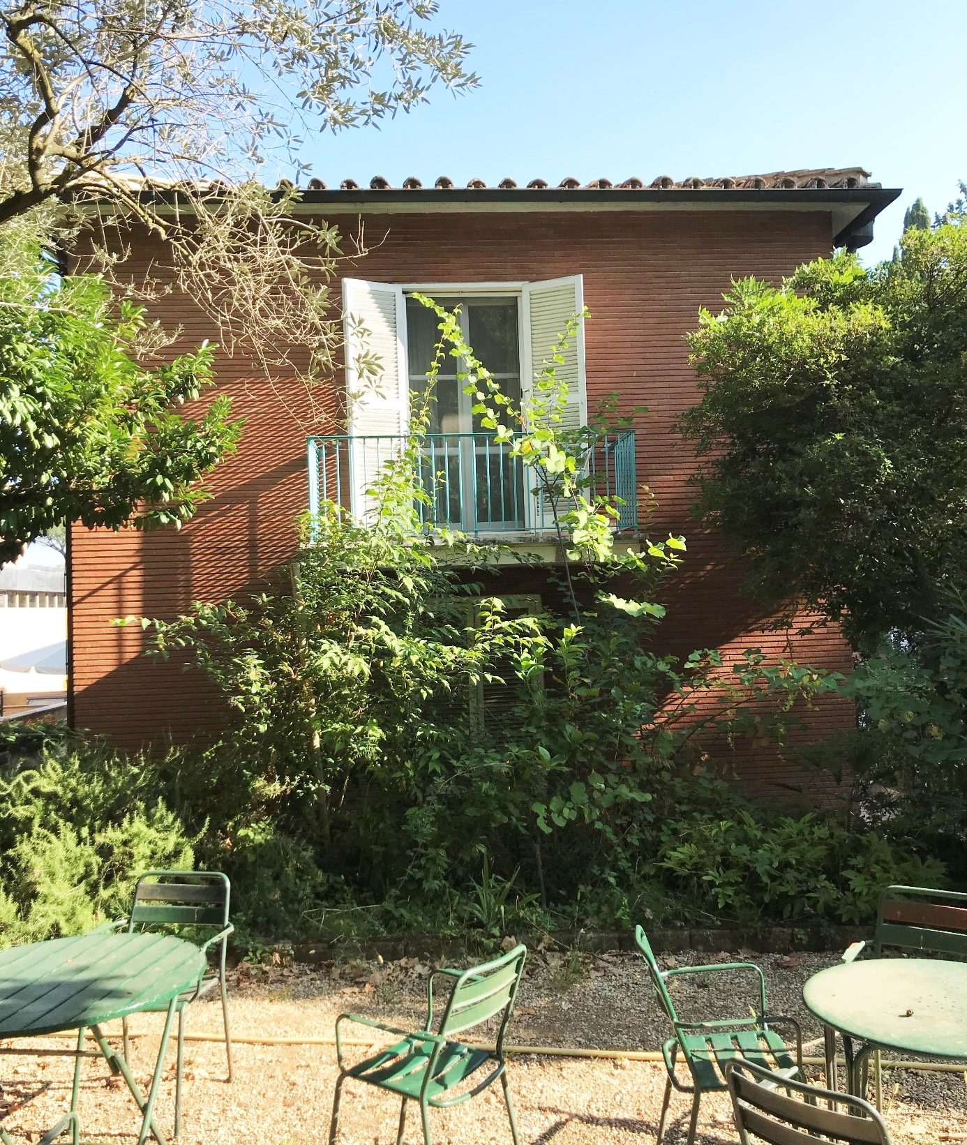 Bild av svenska institutets trädgård och fasad i Rom. Trädgårdsmöbler, buskar, tegelfasad med balkong.