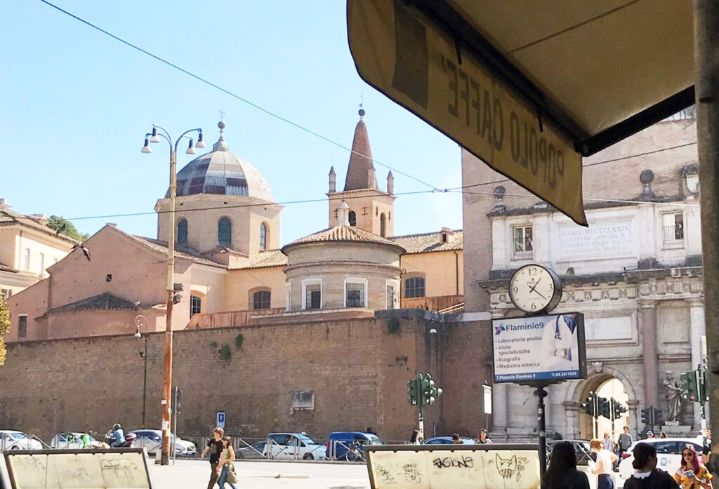 Ett utomhuscafé i solsken utanför Porta del Popolo vid Piazzale Faminio i Rom. Fasader, byggnadsmur, torn och kupol.