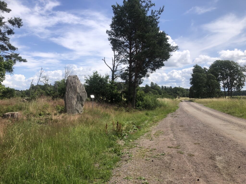 Bilden föreställer en runsten intill en väg.